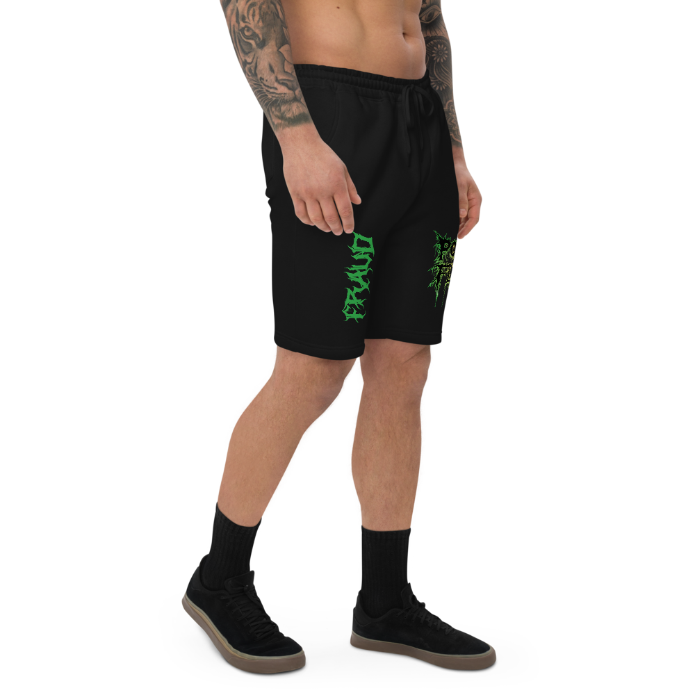 Man wearing black shorts with th ePound of Flesh TX logo outlined in green and yellow on the left leg, and the word Fraud in a gothic fint on the right leg